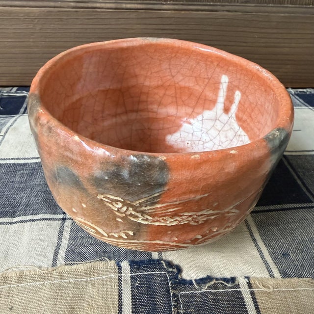 This Japanese matcha bowl is an Aka-Raku chawan from the Shōraku Kiln, finished in a warm, deep red-orange raku glaze....