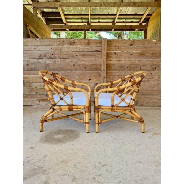 A wonderful pair of vintage mid-20th century rattan barrel lounge chairs featuring sculptural rounded frames, open...
