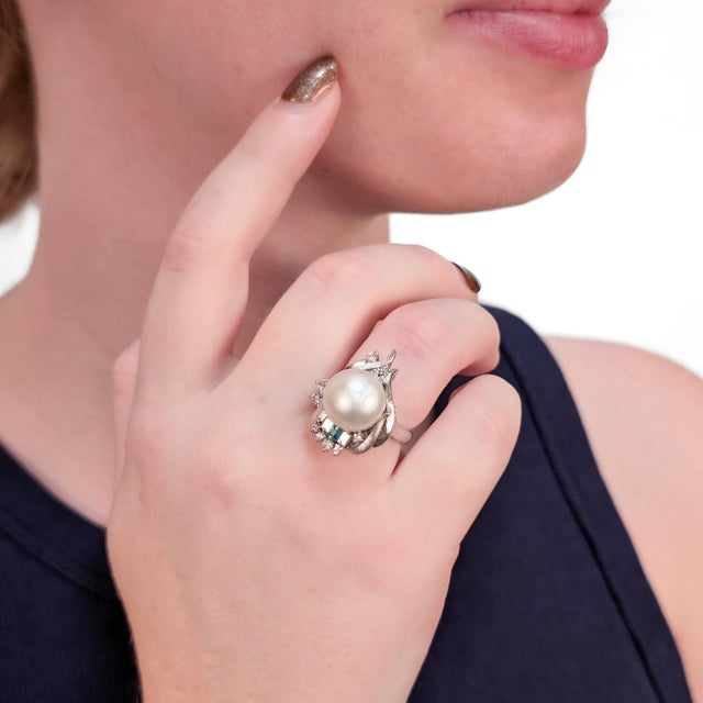 A fine Mid-Century pearl, emerald, and diamond cocktail ring. In .900 platinum. With a high-set central cultured pearl...