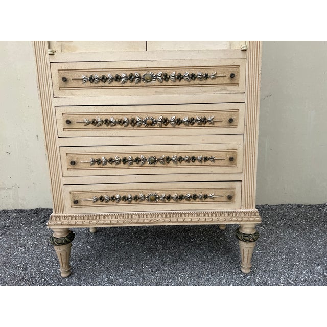 Elegant French Provincial jewelry armoire featuring an antiqued cream crackle finish, ornate floral carved detailing,...
