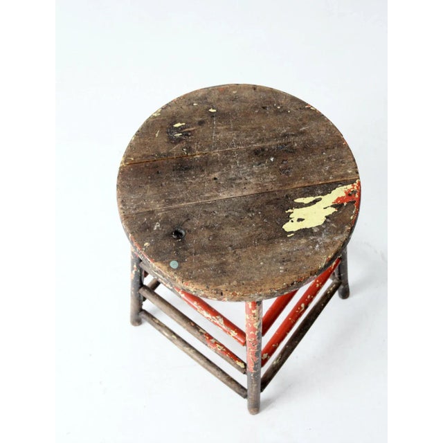 This is a rustic vintage painted wood stool. With red and black painted accents, the wooden farmhouse stool features three...