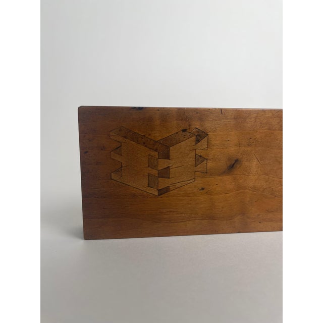 This carpenter’s display piece, crafted from a block of wood with a veneer features two inlaid designs demonstrating...