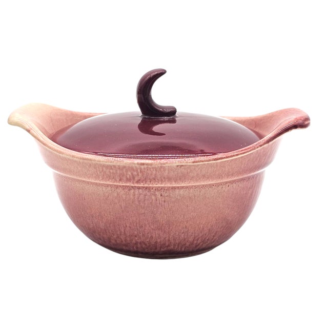 A trio of casseroles, glazed in deep maroon, their crescent handles curving like small moons. Each piece reflects the...