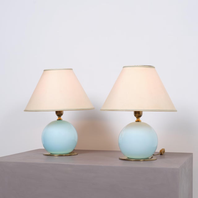 Pair of Italian mid-century table lamps featuring rounded light blue glass bodies, circular brass bases and matching brass...