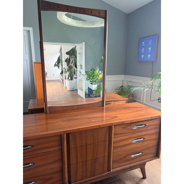 A striking vintage mid-century modern walnut dresser featuring sculptural lines, sleek hardware, and a beautifully...