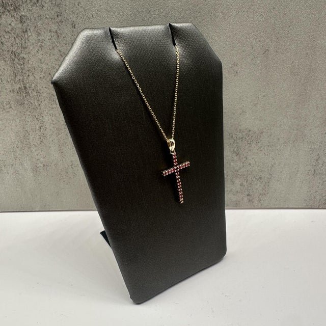 This elegant ruby cross necklace in 14kt yellow gold features 0.20 carats total weight of round rubies, adding rich red...