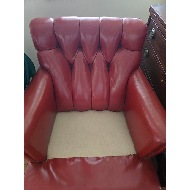 A handsome traditional leather club chair featuring rich oxblood-red leather upholstery, a deeply tufted backrest, rolled...
