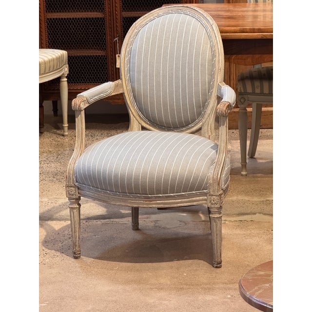 A painted wood arm chair with a shaped upholstered back and seat, featuring curved arms with scroll terminals, carved...