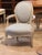A painted wood arm chair with a shaped upholstered back and seat, featuring curved arms with scroll terminals, carved...