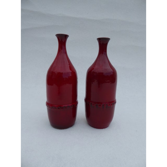 This pair of ceramic vases made by Leon Goossens has red glaze and brown blue glaze on the inside. This piece has an...