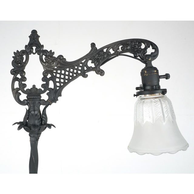 Victorian style floor lamp with a bridge style arm, made of wrought iron with a black finish and a clear and frosted glass...