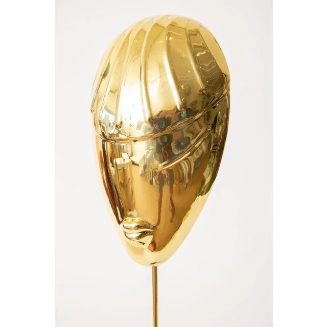 This vintage stylized polished restored tall face mask sculpture sits on a black metal round base and has a brass pole...