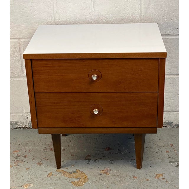 Stylish nightstand crafted in rich walnut, featuring a sleek profile accented by a contrasting white top. Its streamlined...
