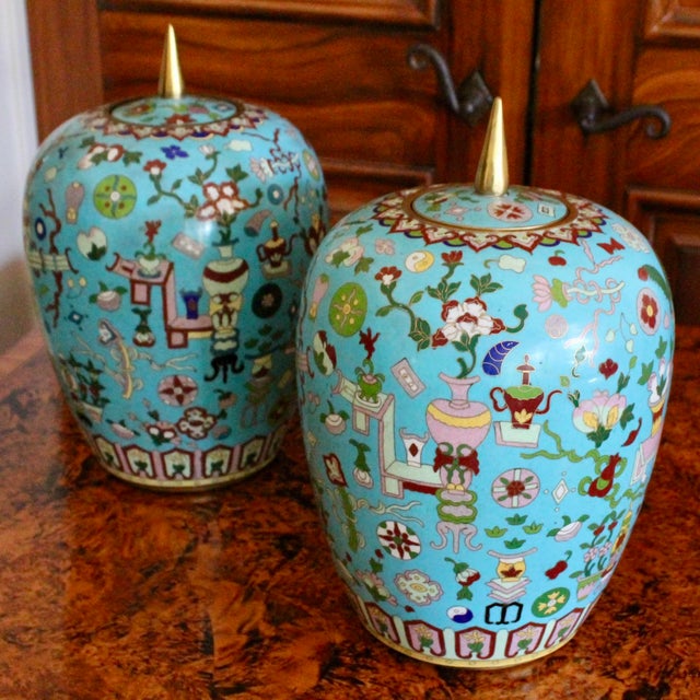 A wonderful pair of brightly colored turquoise cloisonné ginger jars, embellished with the "Hundred Antiques” pattern,...