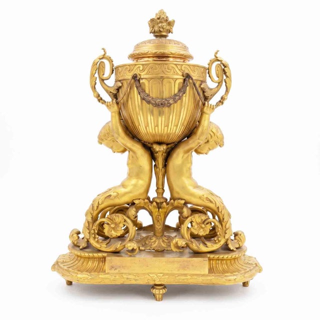 Antique gilded table clock from 1800, in working order. The vertical design features a circular dial set on a two-handled...