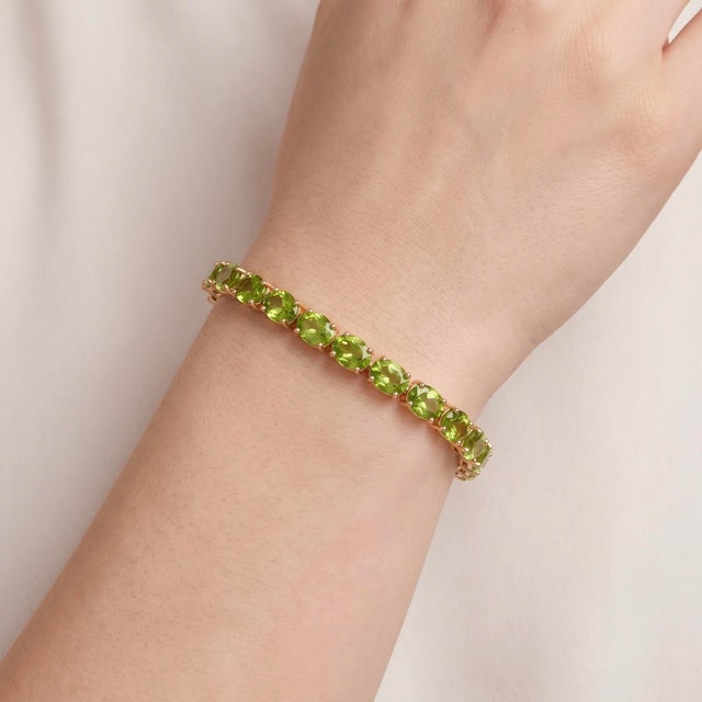 An eye-catching tennis bracelet featuring a continuous row of vibrant lime-green oval peridots set in warm gold-tone...