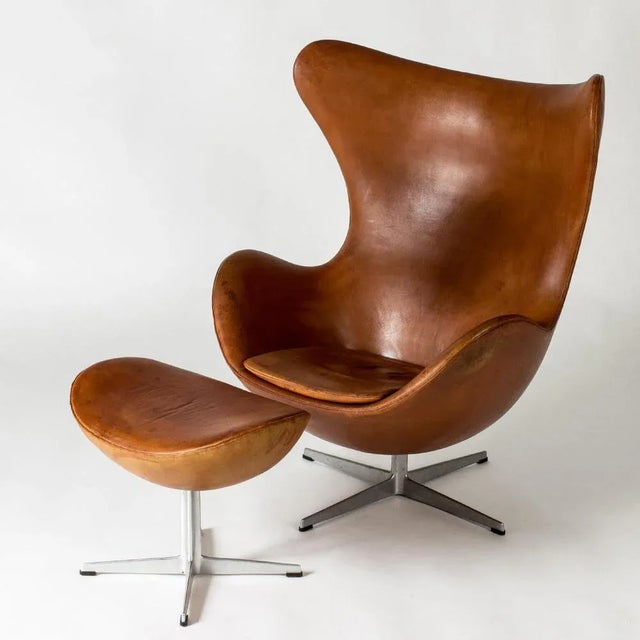 Iconic “Egg” lounge chair and footstool by Arne Jacobsen, upholstered with cognac brown leather. This design was...