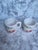 Two festive milk glass mugs with a red and green holiday design by Hazel Atlas. These Mid-Century cups are referred to as...