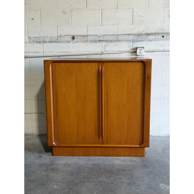 This architectural highboy storage cabinet features seamless tambour doors that glide smoothly into the chassis. The...