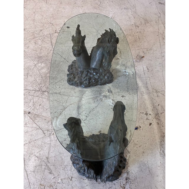 Vintage bronze-tone metal and glass coffee table depicting sculptural wild horses busts beneath a thick beveled glass top....