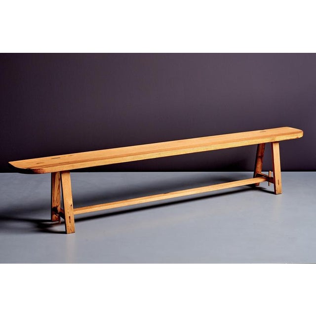 A long solid-wood bench originating from a french monastery, featuring a plank seat on trestle supports with a single...