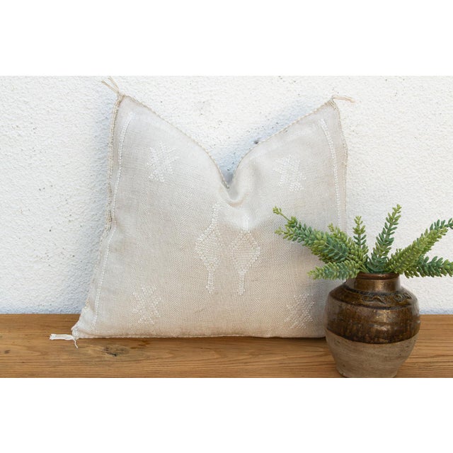 Small X-shaped cross motifs mark the top corners of this handcrafted Moroccan cactus silk pillow, framing a stacked...