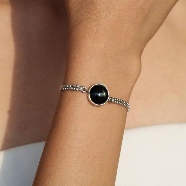A delicate 925 sterling silver bracelet featuring a single round Black Star gemstone (11 mm, 7.6 carats). The deep,...