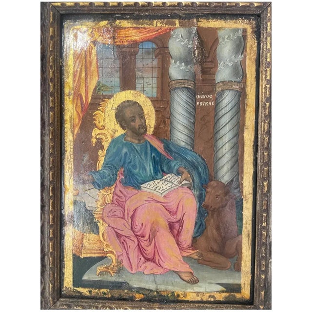 An authentic 19th century Greek Orthodox icon depicting St. Luke the Evangelist, shown seated with his Gospel book and...