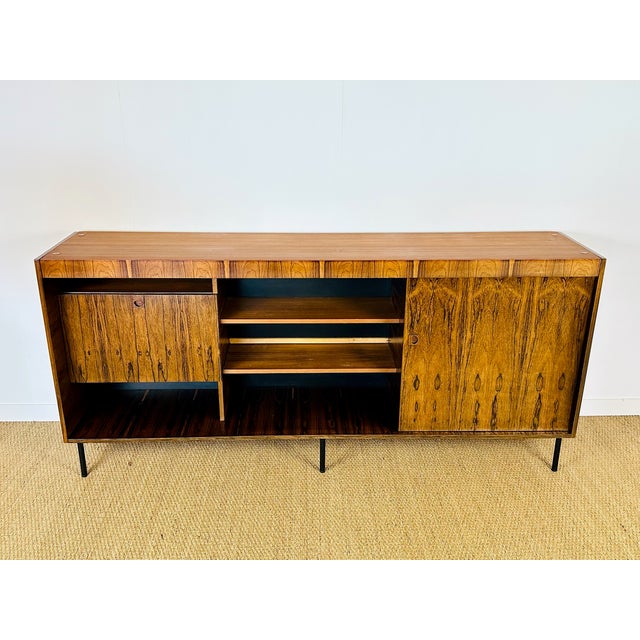A tall, vintage sideboard in exotic wood, with a modernist scandinavian design from the 1960s-70s, resting on slender...
