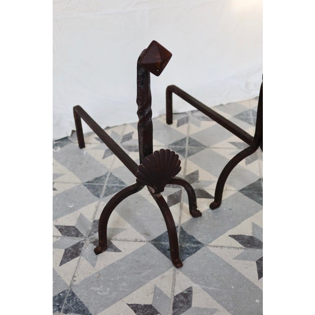 Pair of antique metal and cast iron fireplace andirons, decorated with a shell motif on the front and twisted uprights....