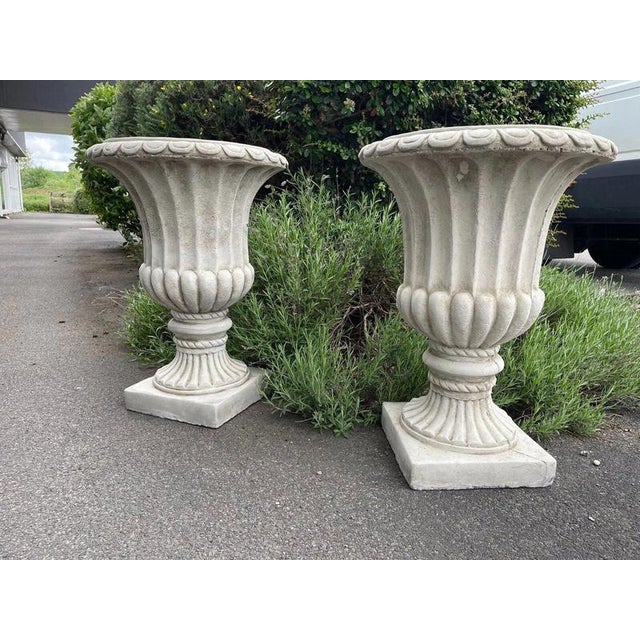 An elegant and highly decorative pair of classical cast stone garden urns, traditionally styled with deeply fluted bodies...