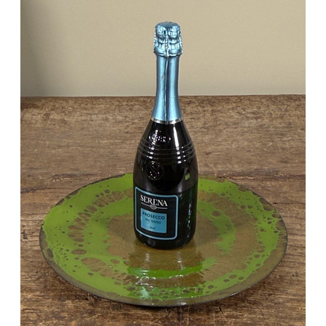 This enamel on copper charger plate features a circular form with concentric decorative patterns rendered in bright green...