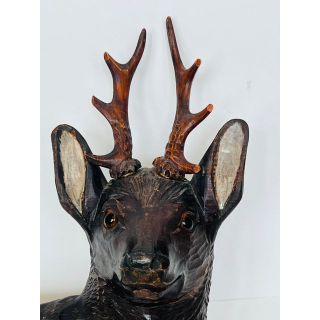 beautifully hand-carved wooden stag sculpture rendered in the traditional Black Forest style, depicting a reclining deer...