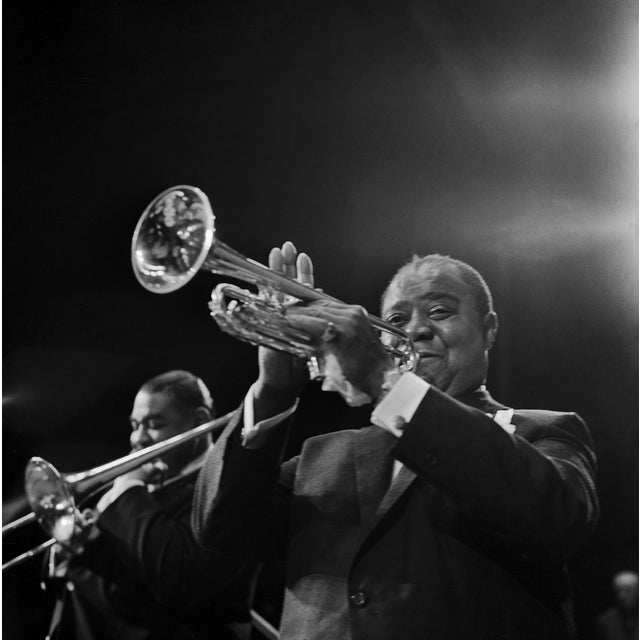 This black-and-white photo captures jazz legend Louis Armstrong playing his trumpet during a performance in Berlin in...