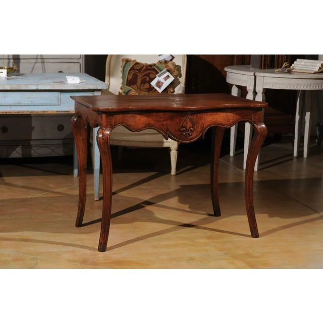 A French Louis XV period Provençale console table from the 18th century, with scalloped apron, stylized fleur-de-lys and...