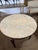 French Neoclassical-style circular black painted table with beige veined marble top, having brass cross banded trim and...