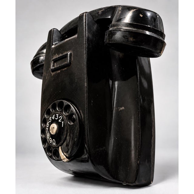 This is a vintage wall-mounting rotary telephone molded in glossy black Bakelite, featuring an integrated handset cradle,...