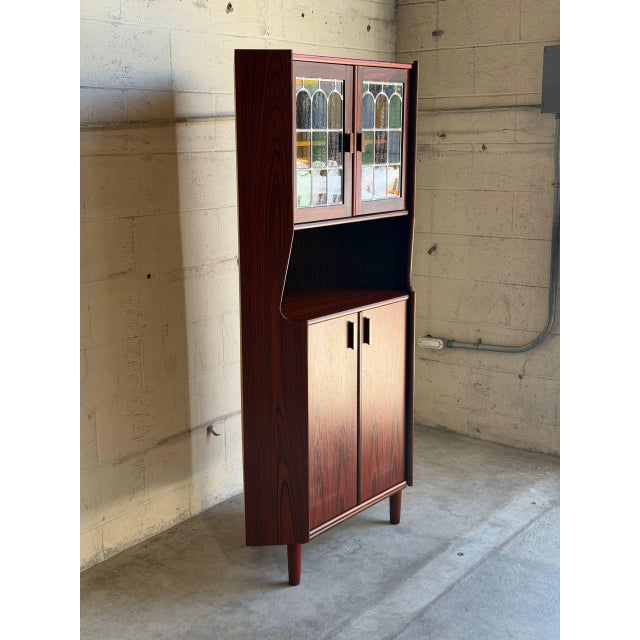 Upper leaded stained glass doors open to reveal display shelving over an open nook and lower solid doors. Round tapered...