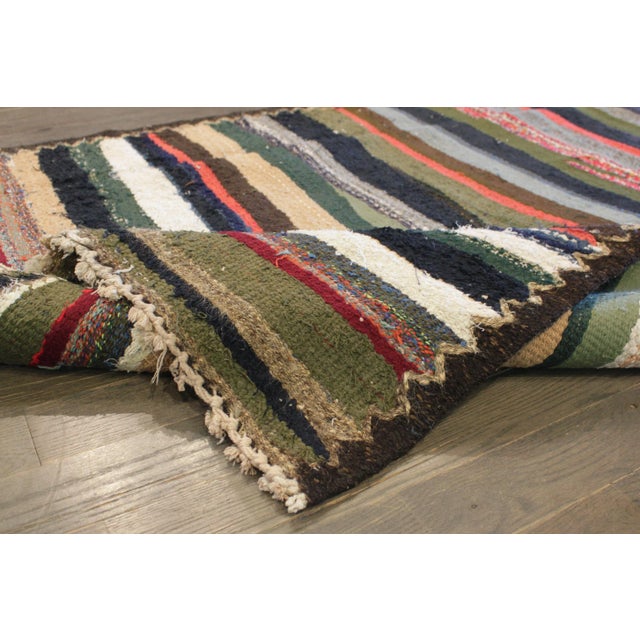 A vintage persian hand-knotted kilim rug with a striped design on a black field. Accents of ivory, green, red and blue...