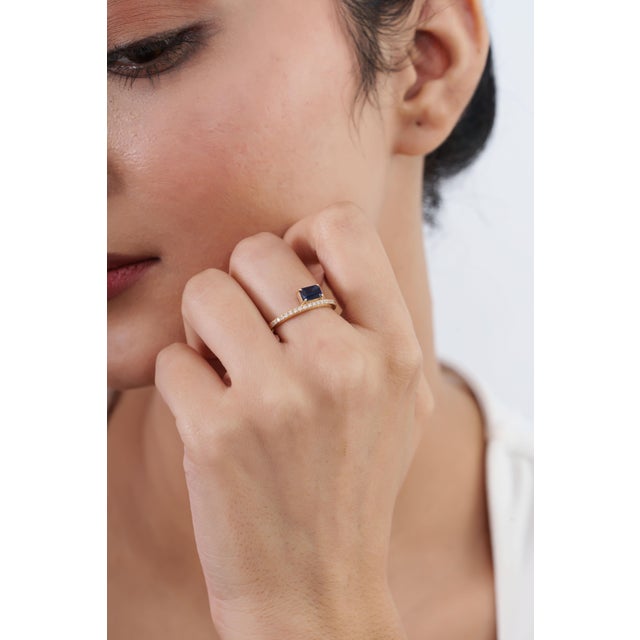 This geometric solitaire band features a 0.57-carat deep blue emerald-cut sapphire, set horizontally in 14k yellow gold....