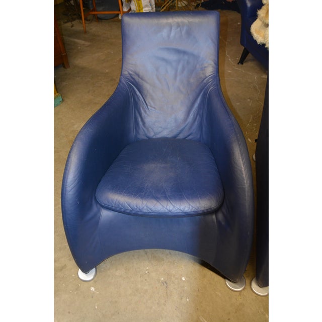 Set of two Montis Lounge chairs and ottomans in a navy blue leather. Seat cushions are removable. Each leg has an attached...
