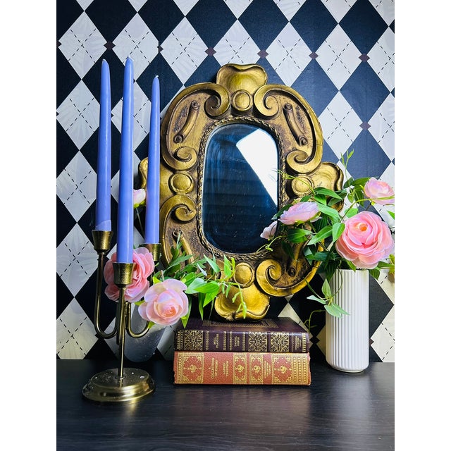 A giltwood wall mirror featuring an ornate Baroque Revival-inspired frame with bold scrolling ornament and an oval mirror...