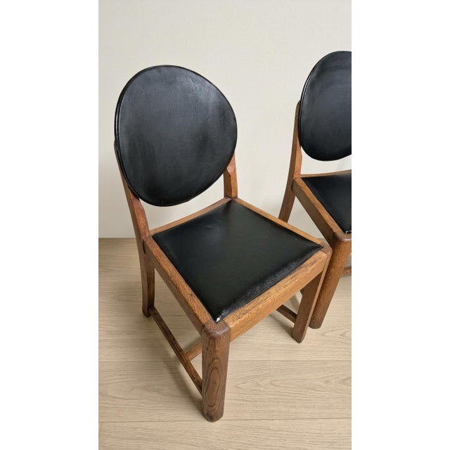 A set of four vintage wooden dining chairs featuring warm-toned wooden frames and distinctive rounded black upholstered...