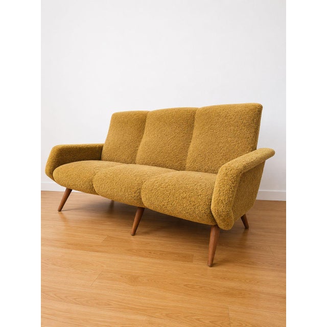 A 1950s three-seater sofa in quintessential Midcentury Modern style, characterized by organic lines and a wraparound...