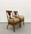 A decorative pair of vintage rattan armchairs featuring sculptural open backs centered by woven wheat sheaf motifs. The...