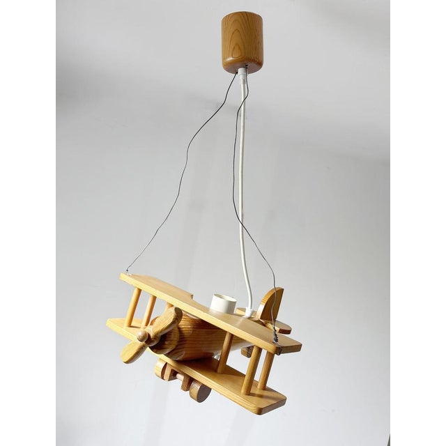 A unique carved pine wood pendant light shaped like a biplane, emblematic of the playful, handcrafted designs of the...