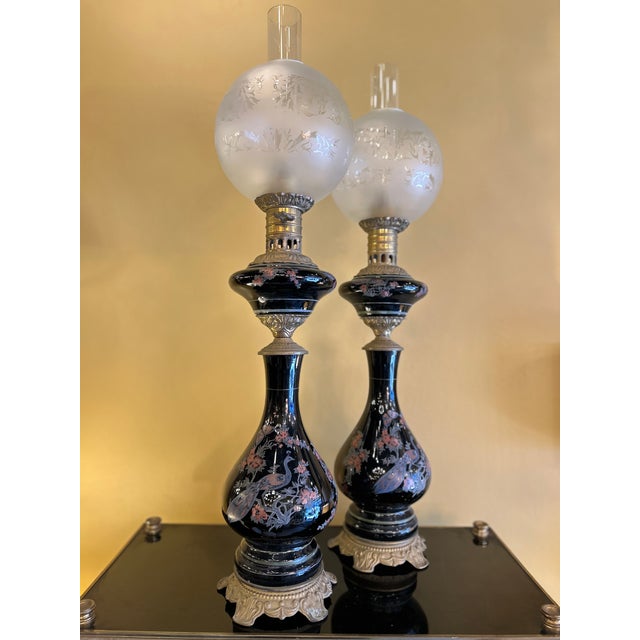 Pair of oil lamps converted to electricity, with black ceramic stems decorated in polychrome with peacocks and flowering...