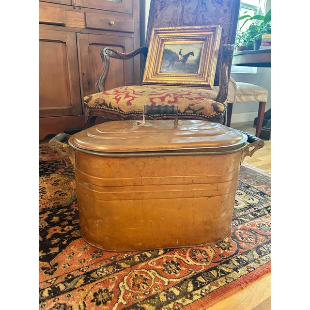 This is an antique copper laundry boiler dating to the early 20th century, featuring a classic oval form, fitted domed lid...