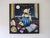 In "Bedtime Story," a whimsical scene unfolds as a cat, dressed in a blue nightgown, sits by an open window, gazing...