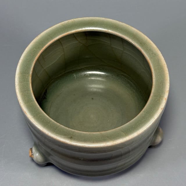 Classic Chinese celadon tripod censer. Horizontal ribbed body, three sturdy short feet, smooth muted green crackle‑glaze,...